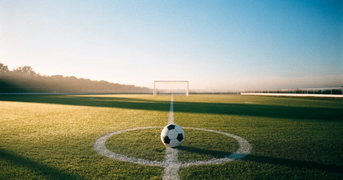 Uma bola de futebol no ponto central de um relvado, à luz da manhã