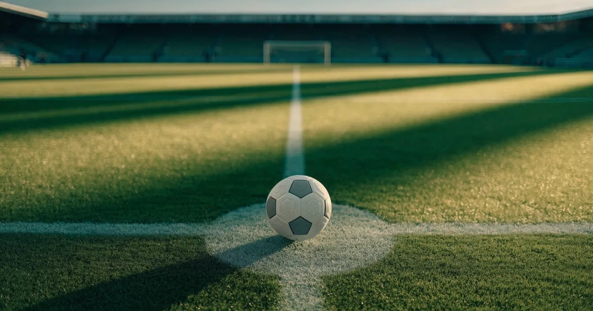 Uma bola de futebol no ponto central de um relvado, à luz da manhã