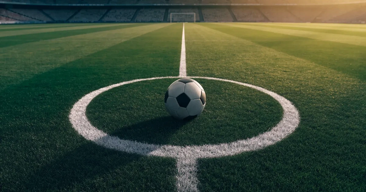 Uma bola de futebol no ponto central de um relvado, à luz da manhã